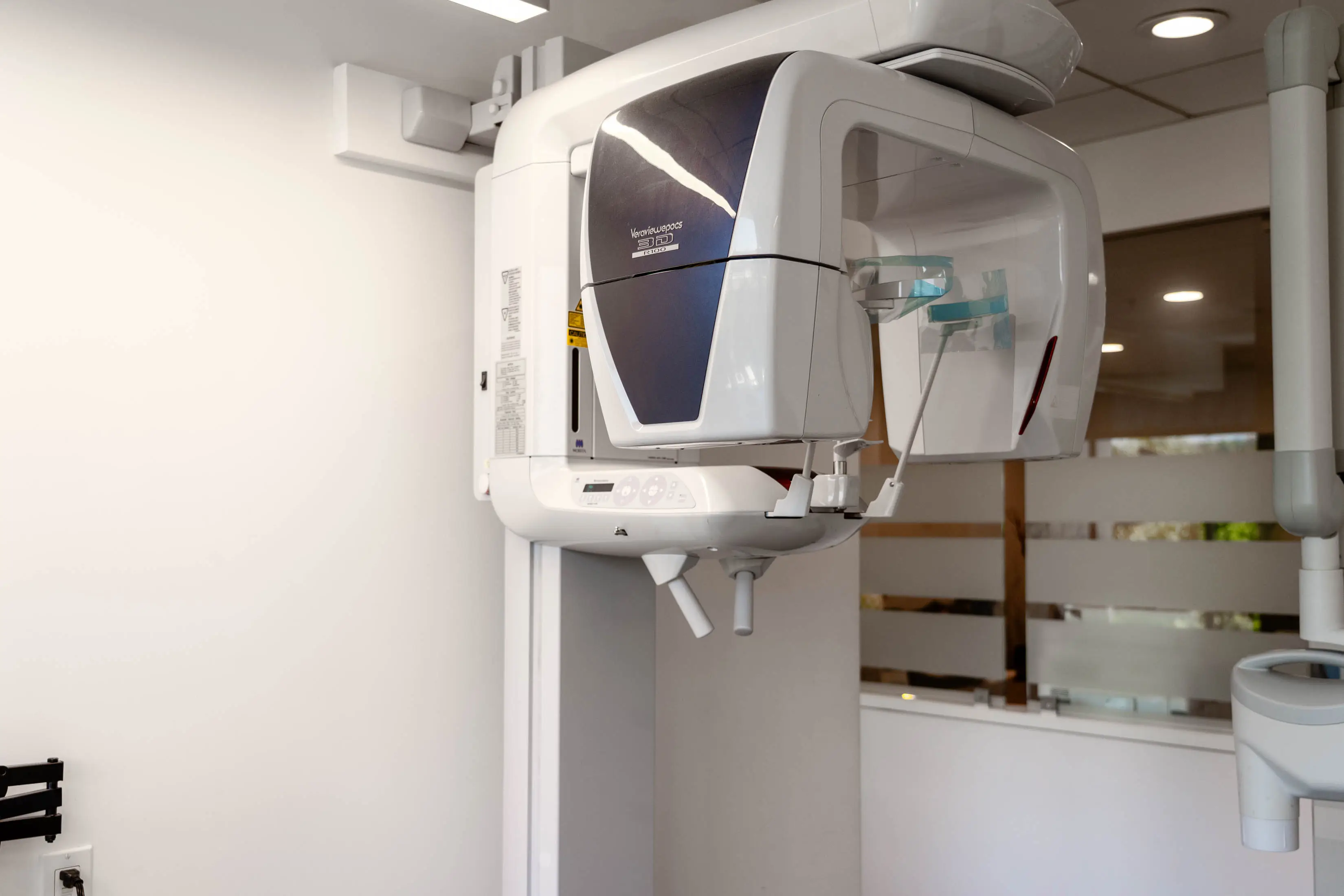 White wall with a medical equipment, a x-ray machine, and a mirror in a room with lights on the ceiling