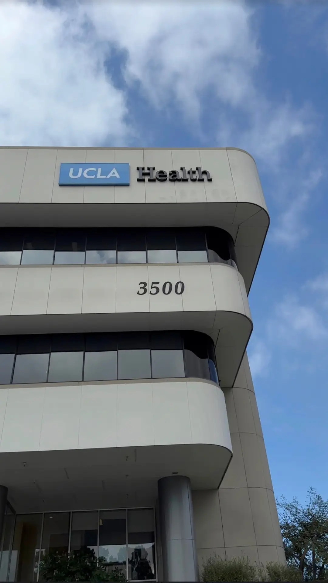 UCLA Health building in, California, with its glass windows, pillars, and name board, surrounded by trees and a sky